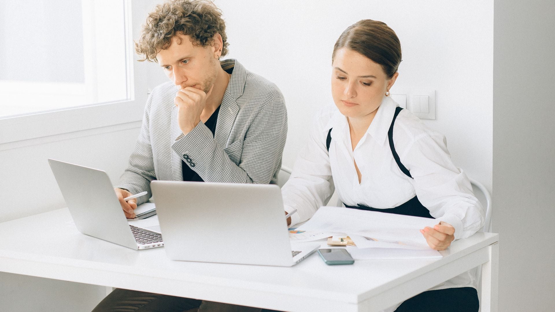 Two colleagues working with laptops and papers at a desk