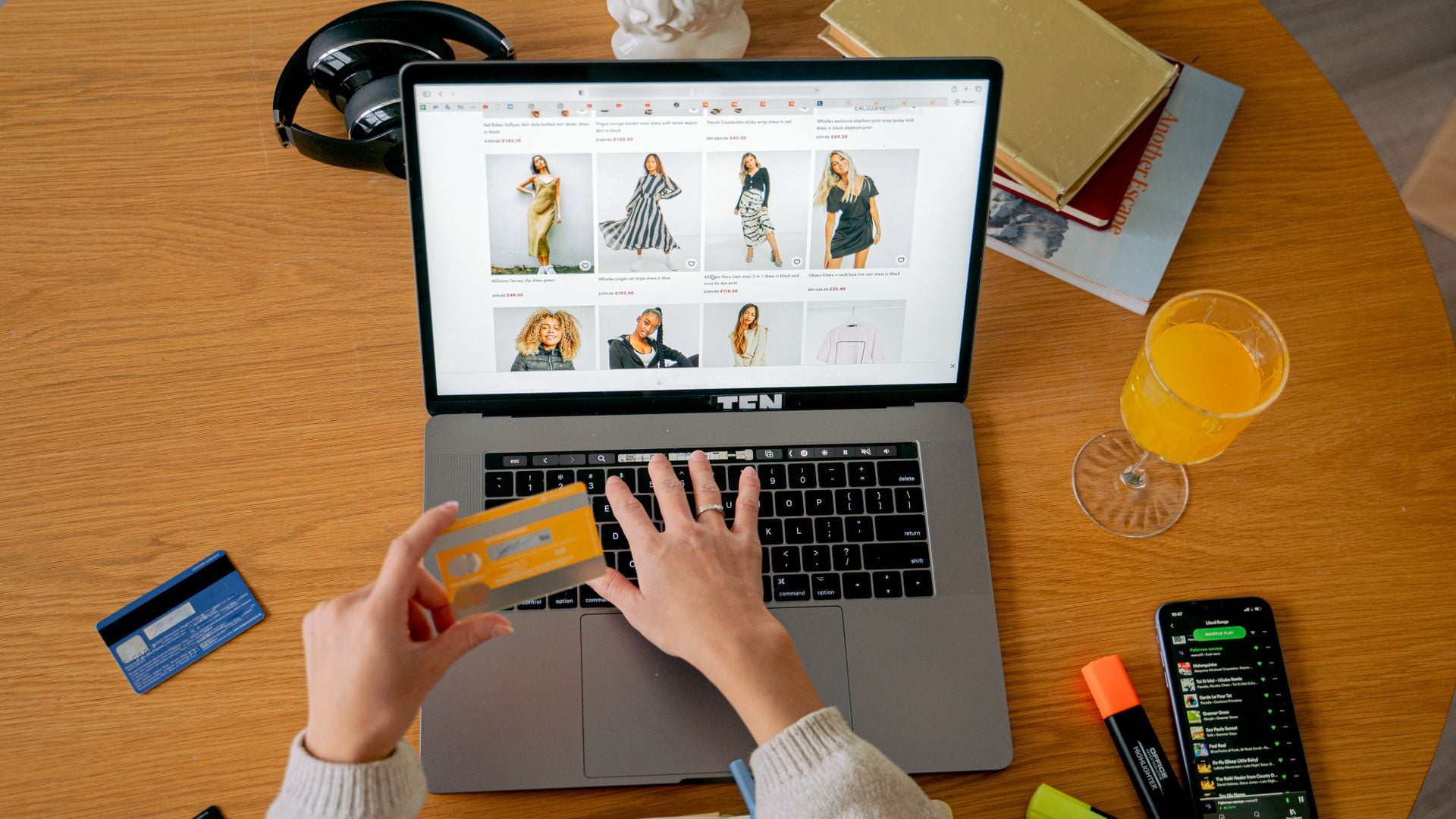 A shopper holds a payment card while browsing clothes on a laptop
