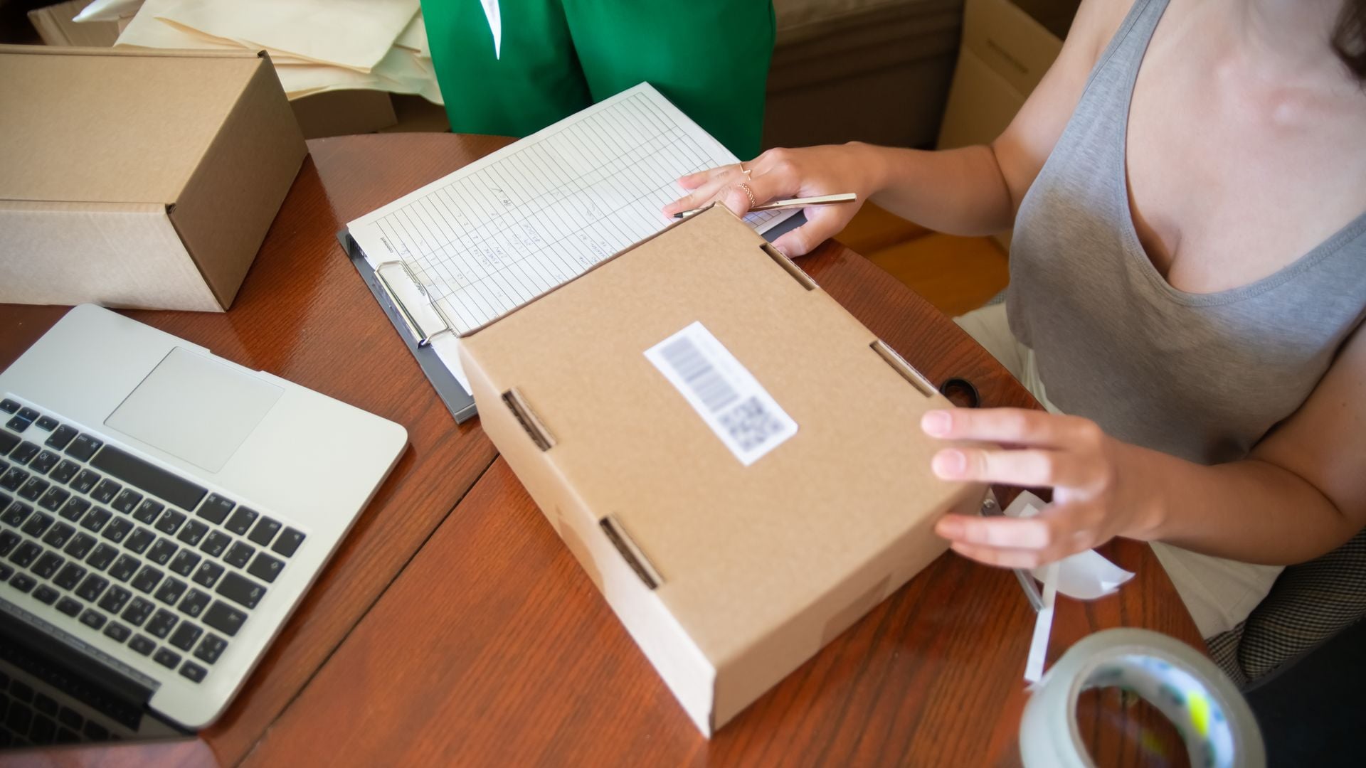 A small-business worker preparing a parcel beside a laptop and order sheet