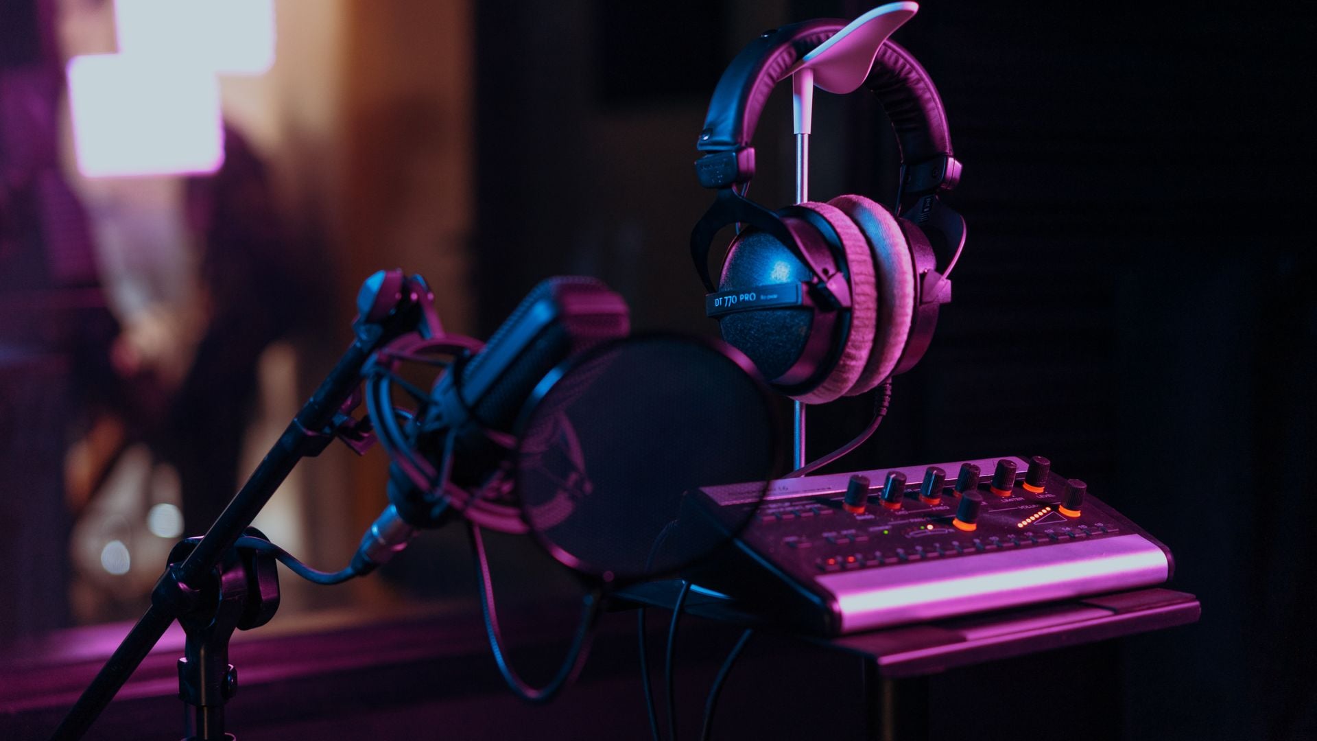 A studio microphone, headphones and audio mixer under colored lighting