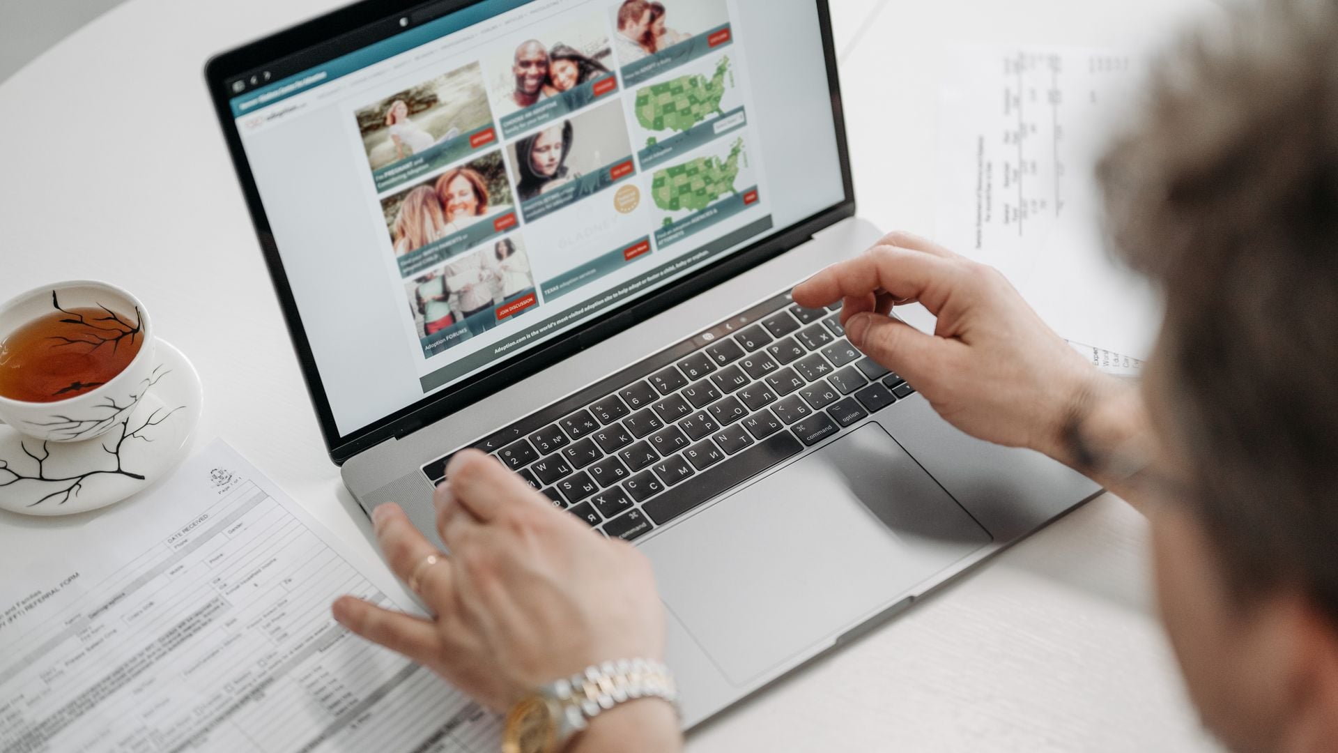 A person browses a website on a laptop beside a cup of tea.
