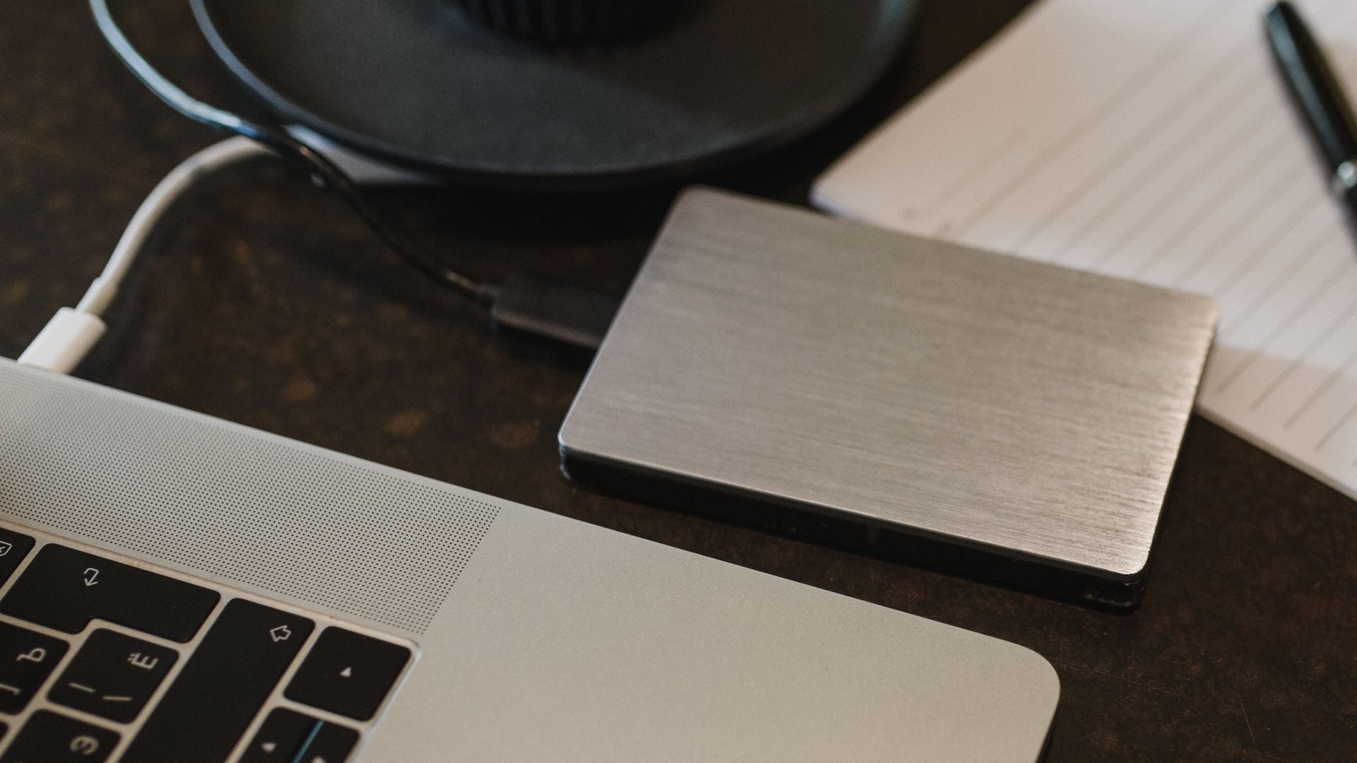 A portable storage drive is connected to a laptop by a cable.