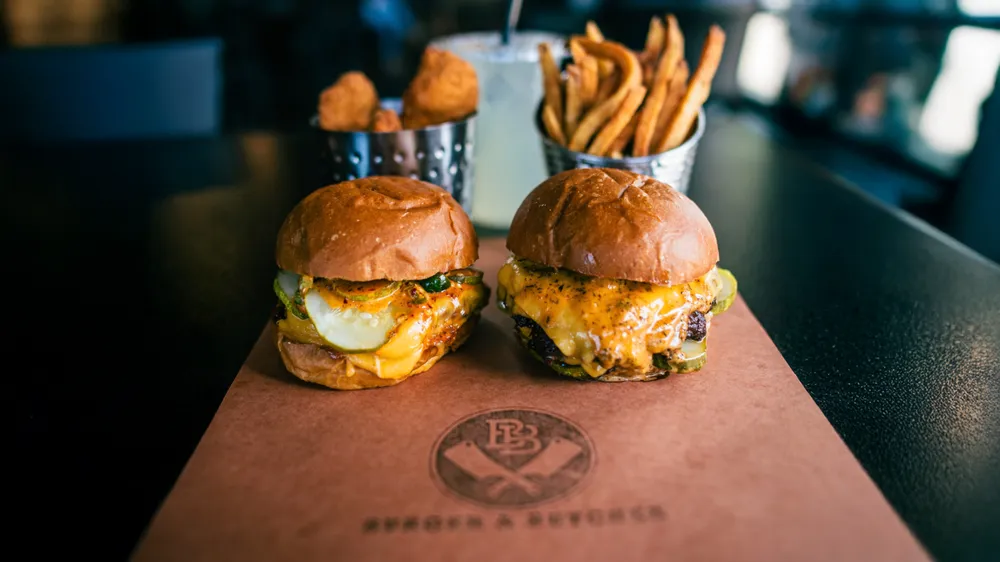 Two cheeseburgers with pickles on branded paper beside cups of fries and chicken nuggets, from Google's business announcement