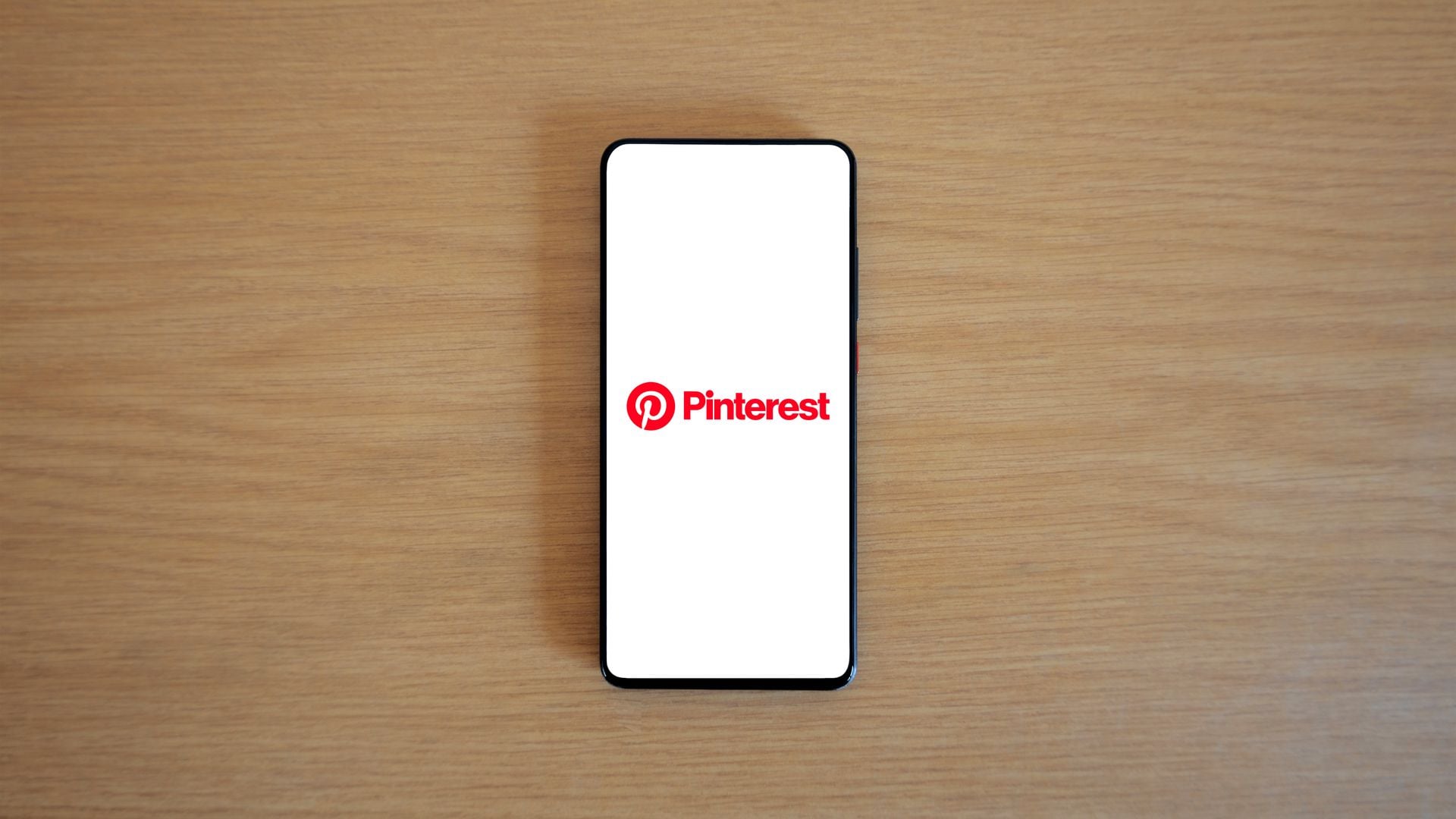 A smartphone displaying the Pinterest logo on a wooden surface