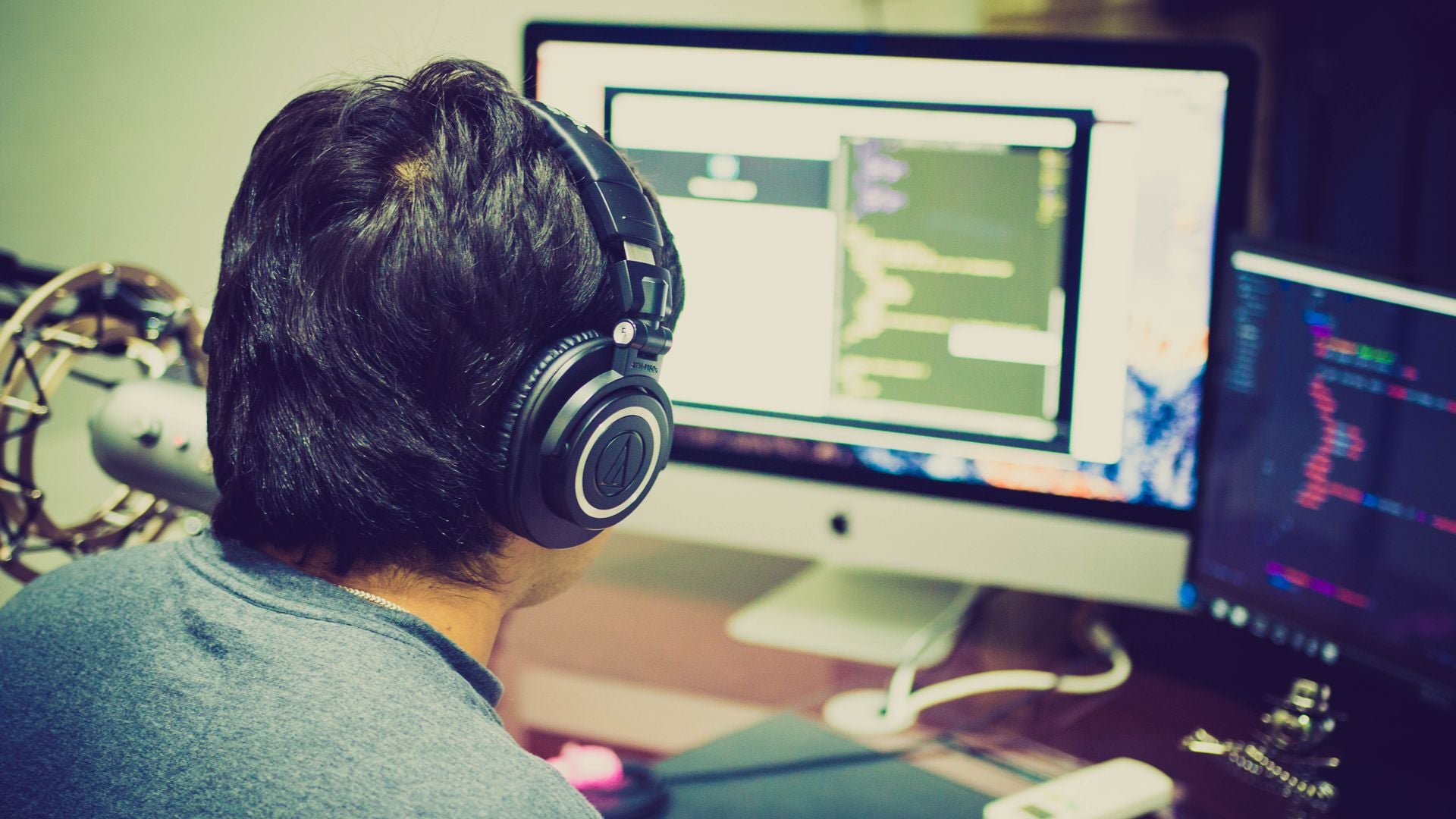 Programmer wearing headphones at a desk with two computer screens
