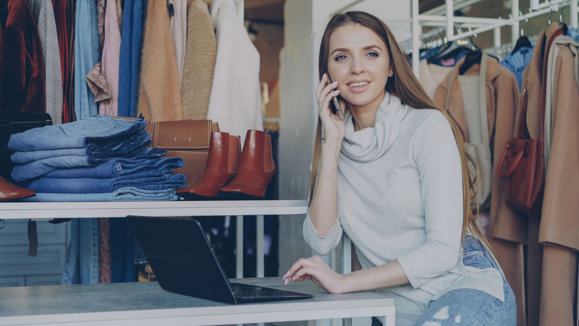 Woman using a laptop and phone in a clothing boutique