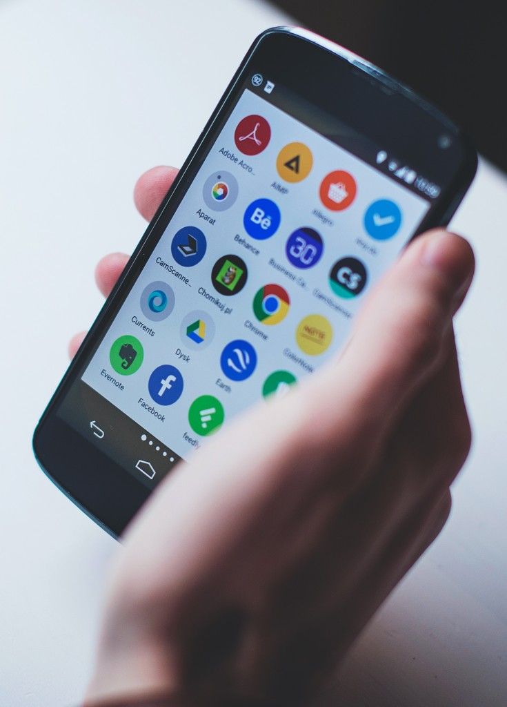 A stock photograph of a hand holding a mobile phone, whose screen is displaying a grid of different apps.