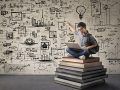 Person with laptop sitting on a giant pile of books and drawing ideas onto a wall behind them.