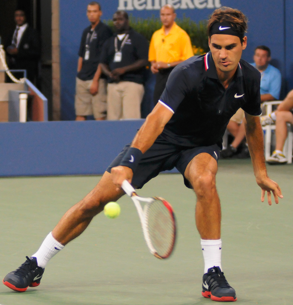 Roger Federer playing in the US Open 2012, crouching down low to hit the ball with his racket.